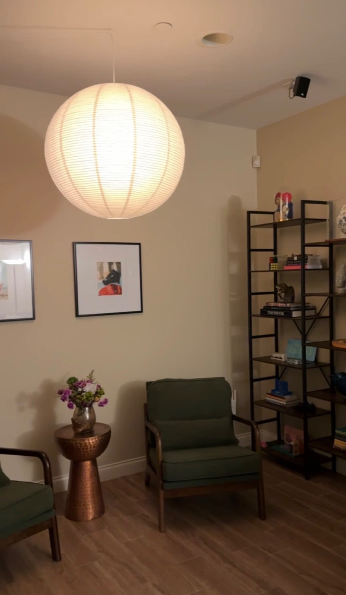Green chairs beside a small table, framed art, and bookshelves